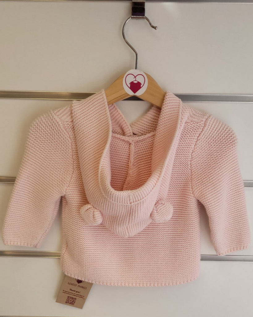 Pink knitted baby sweater on a hanger against a wooden panel background